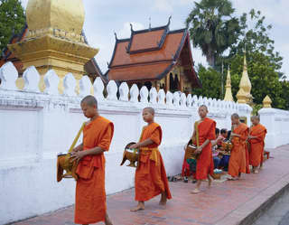 Five orange-robed monks in a Tak Bat procession outside a temple