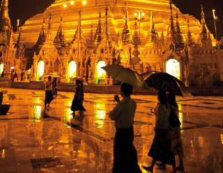 The silhouettes of visitors with umbrellas against the golden glow of Shwedagon Pagoda at night