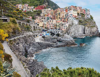 The tiny, picturesque Cinque Terre town of Manarola, with pastel buildings clinging to a rock above a small azure harbour.