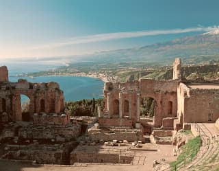 View from the Greek Temple ruins in Taormina down to the azure Ionian coast and up to the smoking, snowy peak of Mount Etna.