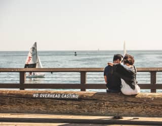 A couple embracing as they sit on a stone wall by the Pacific Ocean