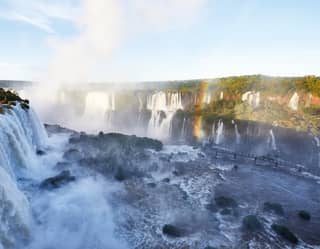 View over lively cascades, from one side of Iguassu Falls' horseshoe shape to the other, where sun dances on the spray.