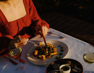 A woman in a red dress enjoys a meal on the terrace in the rosy blush of late sun at a table with oysters and white wine.