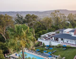 Alongside the pool, hotel first floor terrace tables are surrounded by trees and gardens with distant ocean views