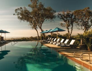 Outdoor infinity pool surrounded by sun beds and blue parasols