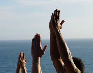 tre persone che alzano le mani in aria e uniscono i palmi in riva al mare