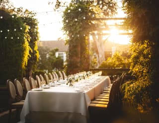 Long banquet table set for a party in hotel gardens at sunset