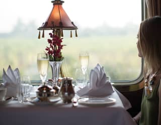 Lady at a table with two champagne glasses gazing out a train window