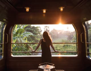 Lady looking out of an open-air train observation carriage at the sunrise beyond