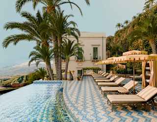 A row of loungers and parasols sit on Villa Timeo's blue and white-tiled terrace by an infinity pool with priceless views.