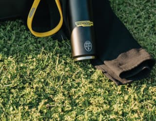 Close-up of a back kit bag with yellow ties and Technogym-branded water bottle lying on lawn.