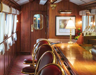 Lamplit train bar car with gleaming polished-wood bar and brass details