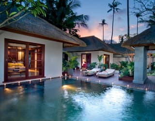 Balinese villas around a freshwater infinity pool surrounded by candles at sunset