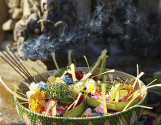 Close-up of fried flowers and burning incense in a reed basket next to a statue