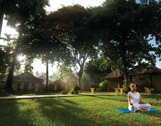 Lady perched on a lush green lawn in the lotus yoga pose at sunrise