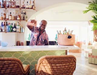 Smiling barman pouring a pink cocktail on a marble bar counter