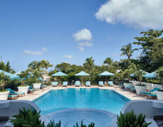 Luxury outdoor pool surrounded by sun beds and parasols under blue skies