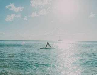 Sun beams down on Baie Longue's waters, where a woman practices yoga on a paddleboard, balancing in a downward-dog pose.