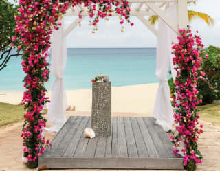 Pink flowers of climbing bougainvillea trace the edge of a wedding arbour, in front of the bay's white sand and turquoise sea