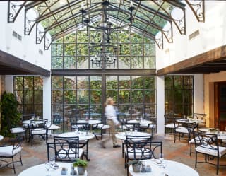 Restaurant with a glass apex ceiling and glass walls surrounded by lush foliage