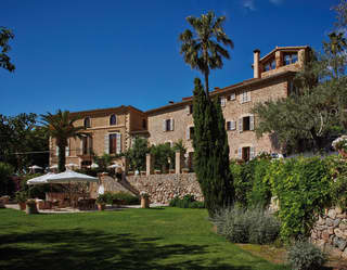 The honey stone of La Residencia's facade glows warm under the pure blue of a cloudless sky. Large parasols shade the patio