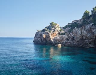 The still sea is a palette of aquamarine, turquoise and cobalt in the small cove at Cala Deia, surrounded by limestone cliffs