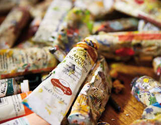 A jumbled pile of an artist's oil paints. Some of the tubes misshapen from use, all with smudges of many colours