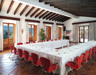 Linen-topped banquet tables set for a meeting in a 'U' formation with red chairs