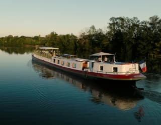 View down a wide, calm waterway, where the Coquelicot glides on the right hand side, brushing the water with tiny ripples.