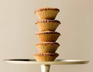 Close-up photograph of five baked pastry mince pies stacked in a tower on a silver cake stand, seen from the side.