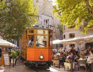 The vintage tram trundles between citrus trees and outdoor café tables in the heart of Soller