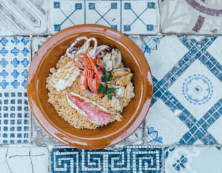 A fresh seafood dish in a simple brown bowl on old blue-and-white ceramic tiles