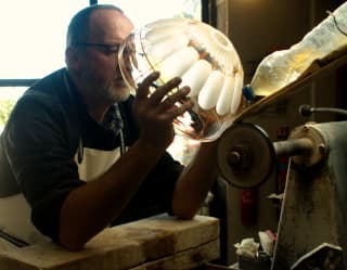 Glassmaker Sébastien Denizard holds a blown glass bowl against an etching machine, creating stunning, intricate patterns.