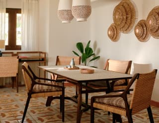 Two white pendant lights hang above a table and four wicker chairs in an elegant dining area with warm and traditional tones.