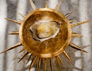 A raw oyster with pineapple and lemongrass is served in a theatrical gold dish with a halo of spikes at Woodend restaurant.