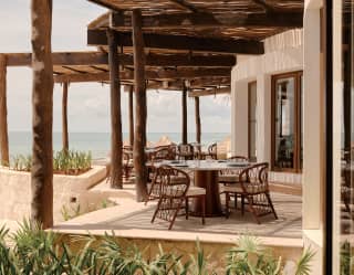 View of the stepped outdoor terrace of Woodend, where tables sit in the shade of wicker pergolas, just a step from the beach.