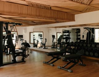 A large gym with a wall-length mirror, weights rack and fitness equipment provides guests with all they need for a workout.