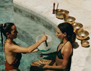 Looking down on a therapist as she guides a guest through meditation in the Spa pool, with brass bowls lined on the poolside.