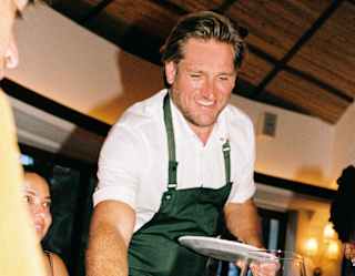 Smiling, Chef Curtis Stone delivers a plate of grilled, wood-fired ribeye steak to a table of diners at Woodend.