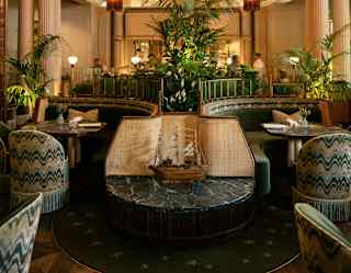 A sailing ship ornament sits on a marble end table between two booths positioned beneath four giant amber glass chandeliers.