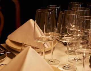 Close-up of a dining table with two plates topped with folded napkins, cutlery and a selection of clean, elegant wineglasses.