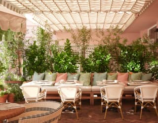 A trellis and potted shrubs promote a country garden feel to the dappled terrace, picked up in pink and green bench cushions.