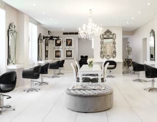 Bright marble floored hair salon lined with black leather salon chairs