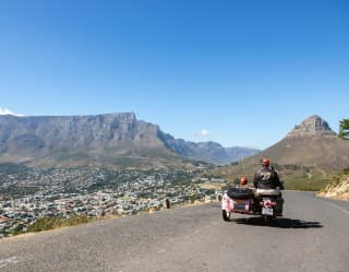 Guests enjoying a sidecar adventure travel an empty road towards the valley dividing Table Mountain and Lion's Head trails.