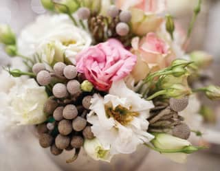 A rustic, floral bouquet of woody Brunia Nodiflora and white and pink lisianthus blooms with green buds in a silver urn.