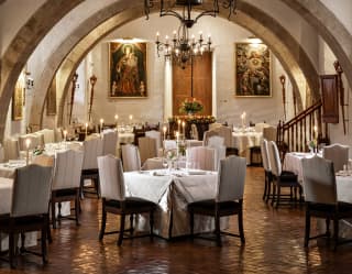 Candles glow in El Tupay's cavernlike dining room with white tables and two chandeliers, hanging between wall arches.