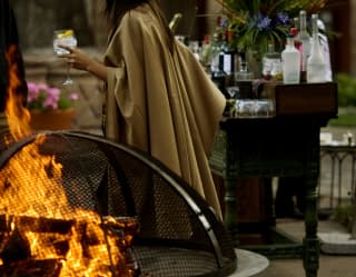 A woman holding a cocktail, standing near the fire pit in the courtyard