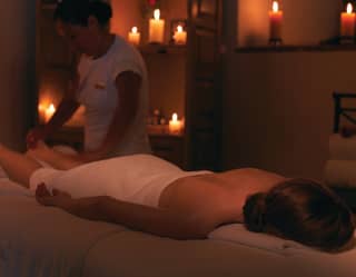 Spa therapist massaging the legs of a guest in a candlelit spa room