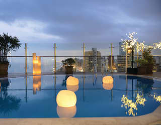 Balcony pool in evening light with floating lanterns and the cityscape beyond