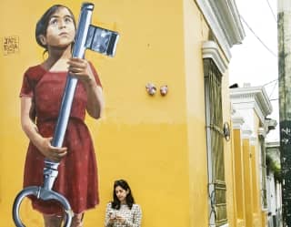 A woman looking at her phone, leaning against a yellow wall in Barranco, Lima